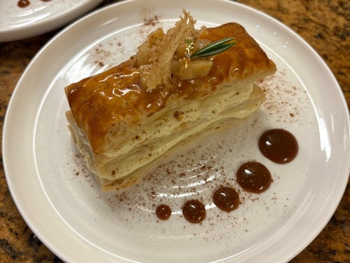Mille-Feuille dessert with caramel glaze, garnished with crispy sugar and rosemary.