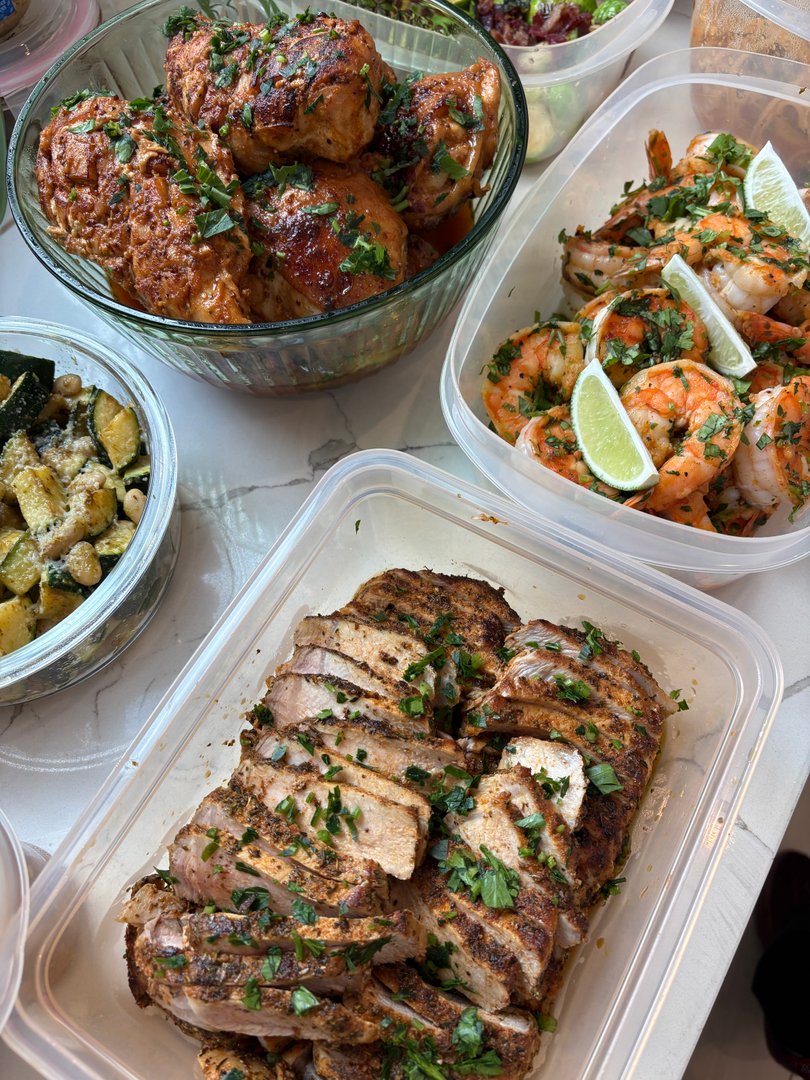 Assorted meal prep containers with chicken, shrimp, pork, and zucchini salad.