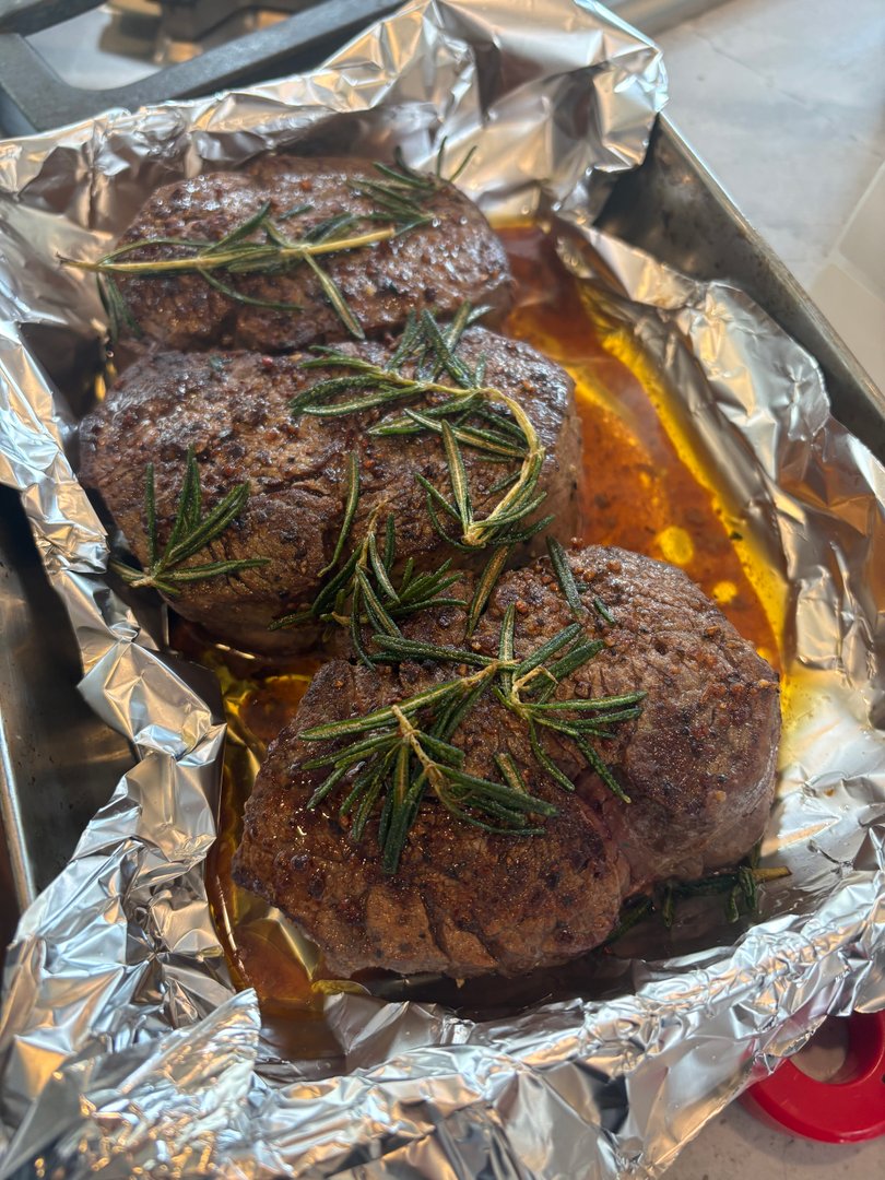 Rosemary-crusted beef filets roasting in foil-lined pan.