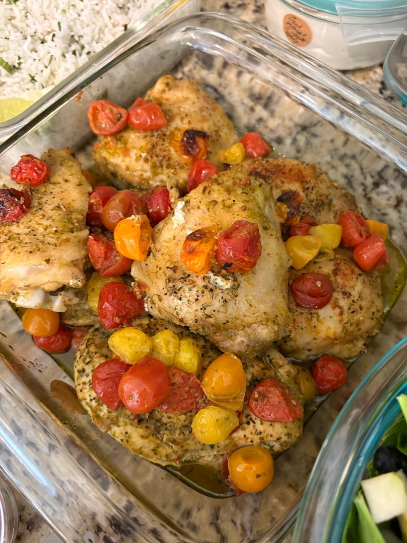 Baked chicken thighs with roasted cherry tomatoes in a glass container.
