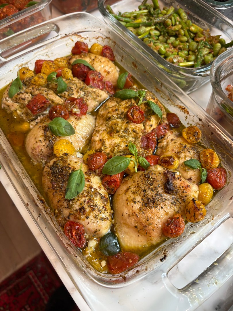 Baked chicken breasts with cherry tomatoes and fresh basil in a glass dish.