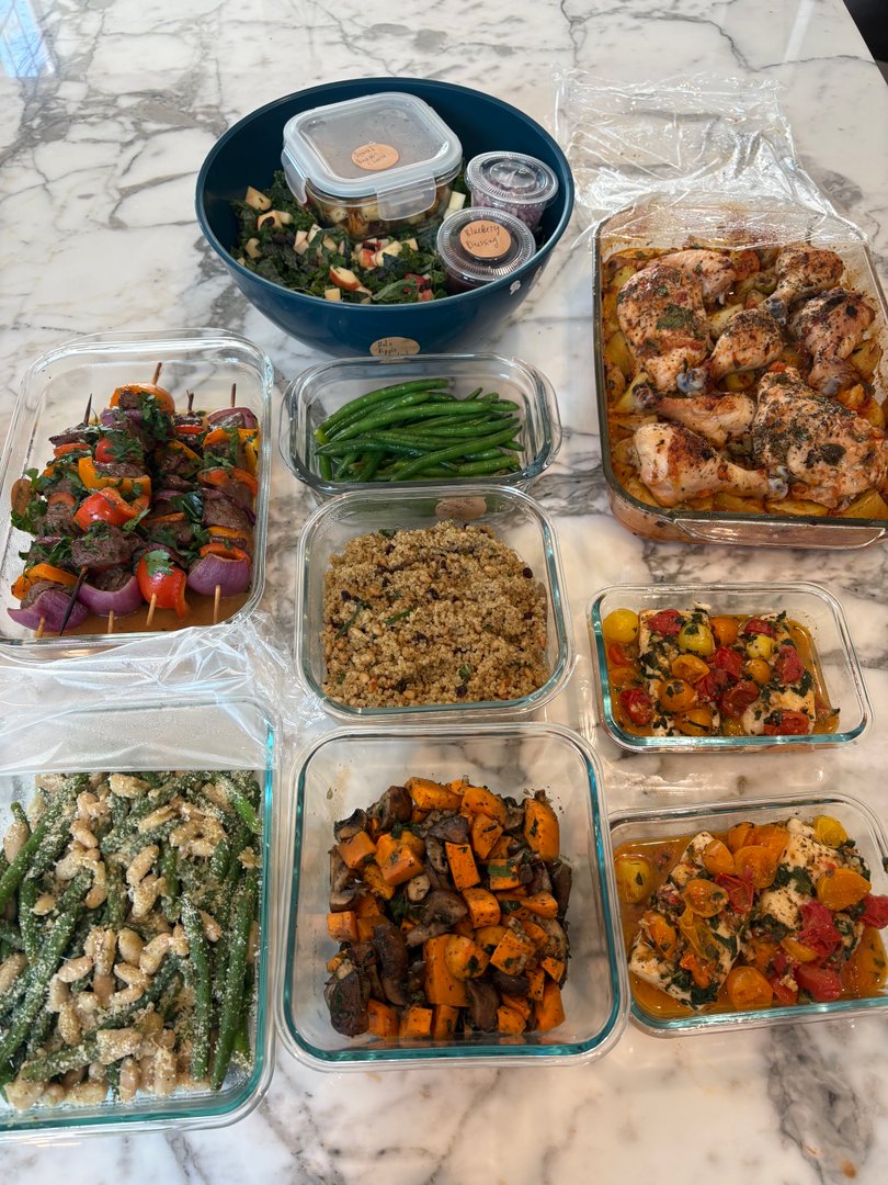 Various meal prep containers filled with Cuban-style dishes on a marble counter.