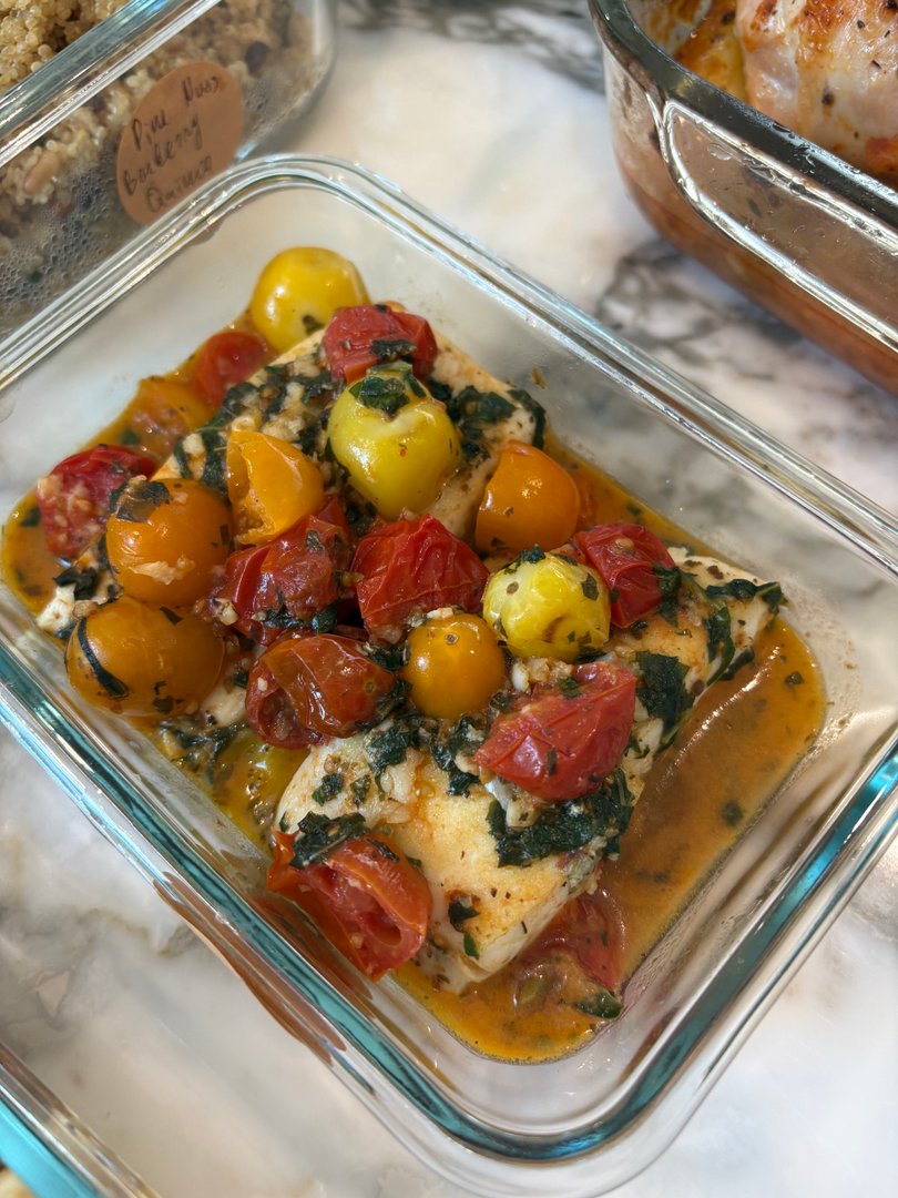 White fish fillets topped with colorful cherry tomatoes and herbs in a glass container.