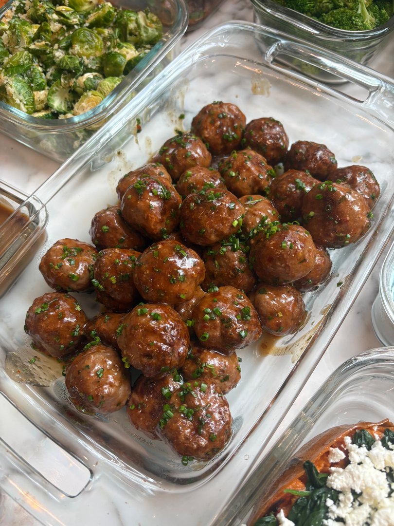 Glass dish filled with glazed meatballs and chives.