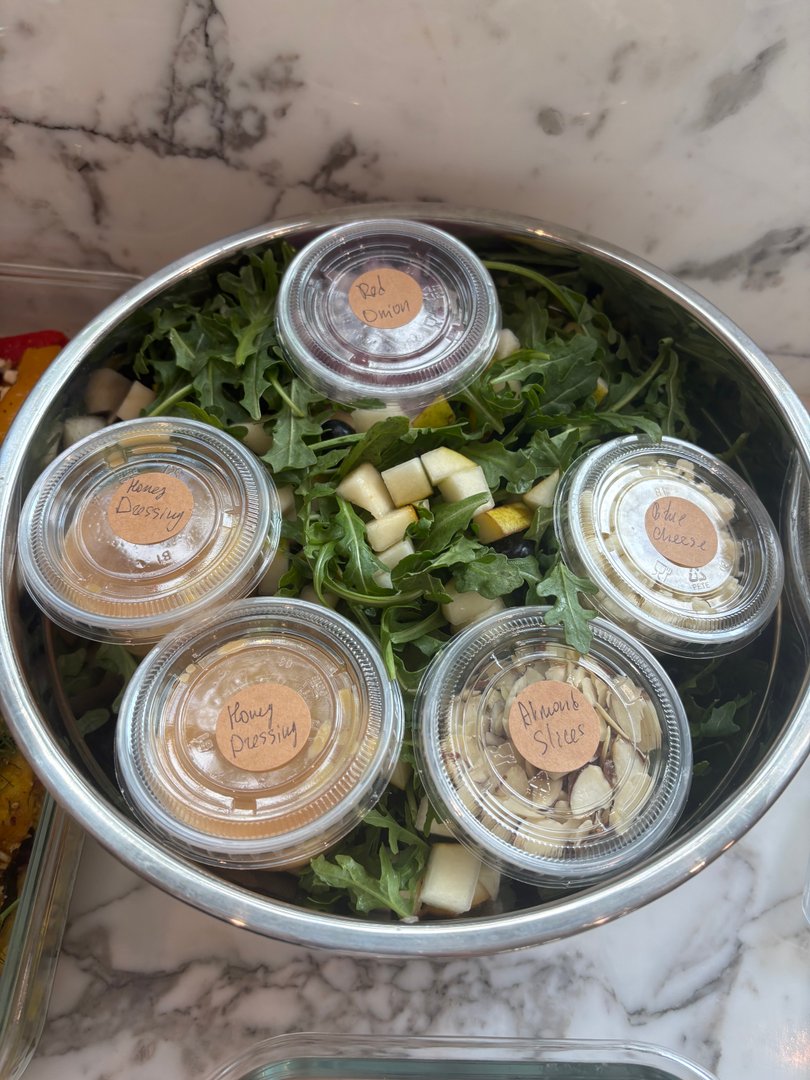 Large salad bowl with arugula, pears, and dressing containers.