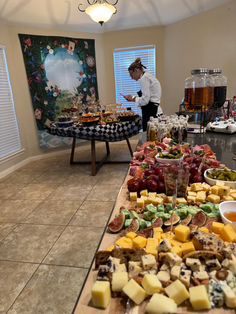 Chef Ana preparing food with charcuterie boards in foreground, Alice in Wonderland backdrop