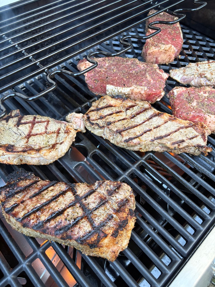 New York strip steaks grilling on an outdoor barbecue