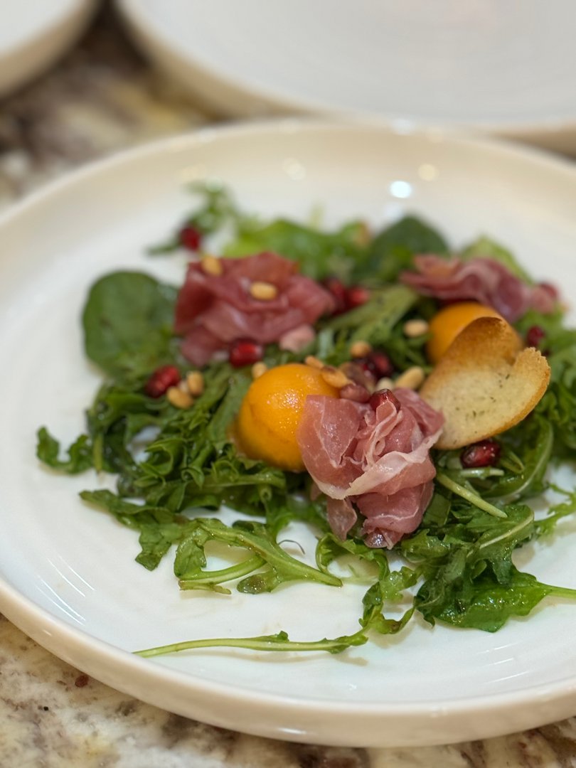 Close-up of fresh salad with prosciutto, melon, pomegranate, pine nuts, and croutons.