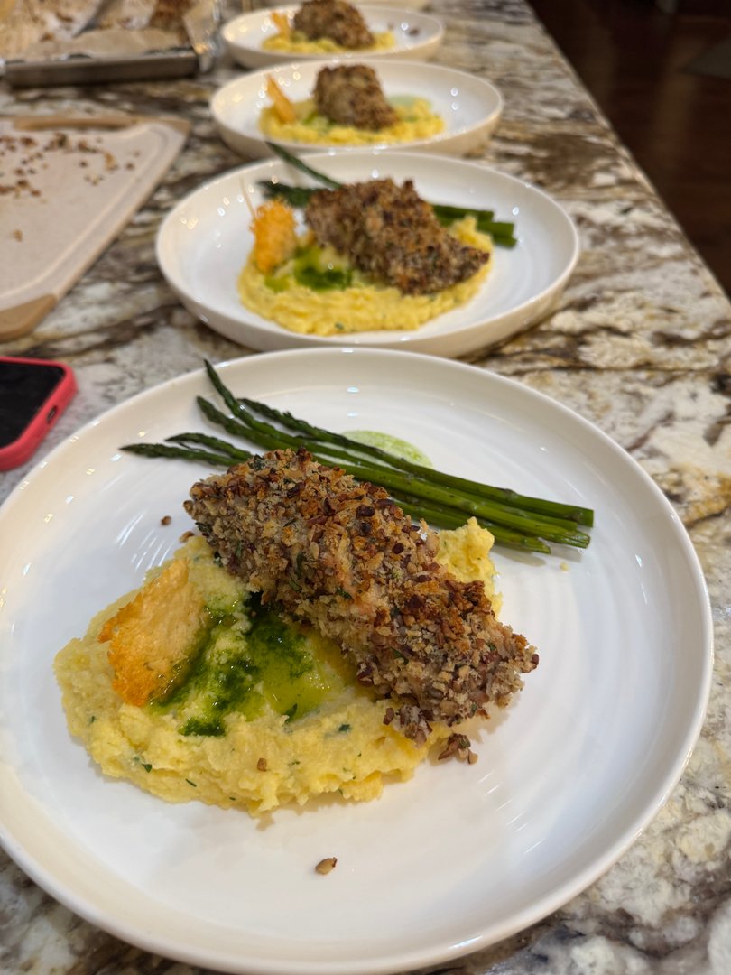Plated pecan-crusted fish with creamy polenta, asparagus, and green herb oil.